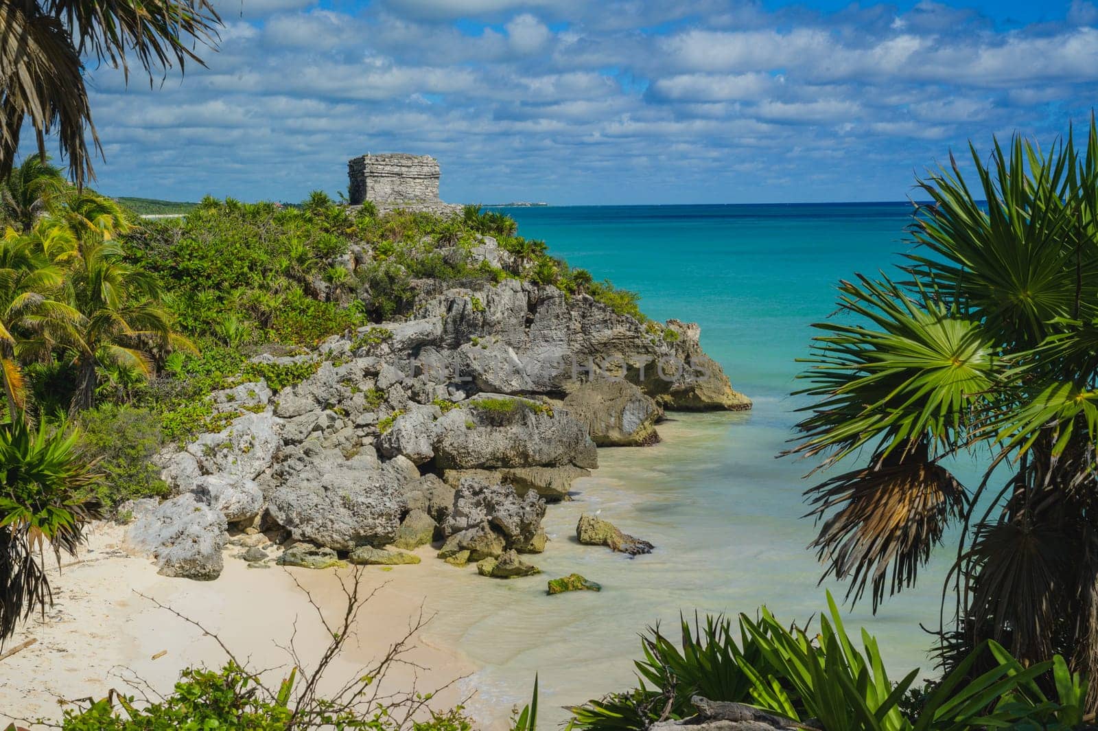 Ruins of Tulum, Mexico and a palm tree overlooking the calm Caribbean Sea in Quintana Roo, also known as the Riviera Maya. Blue sea and cloudy sky in the Mexican jungle. Travel and tourism.