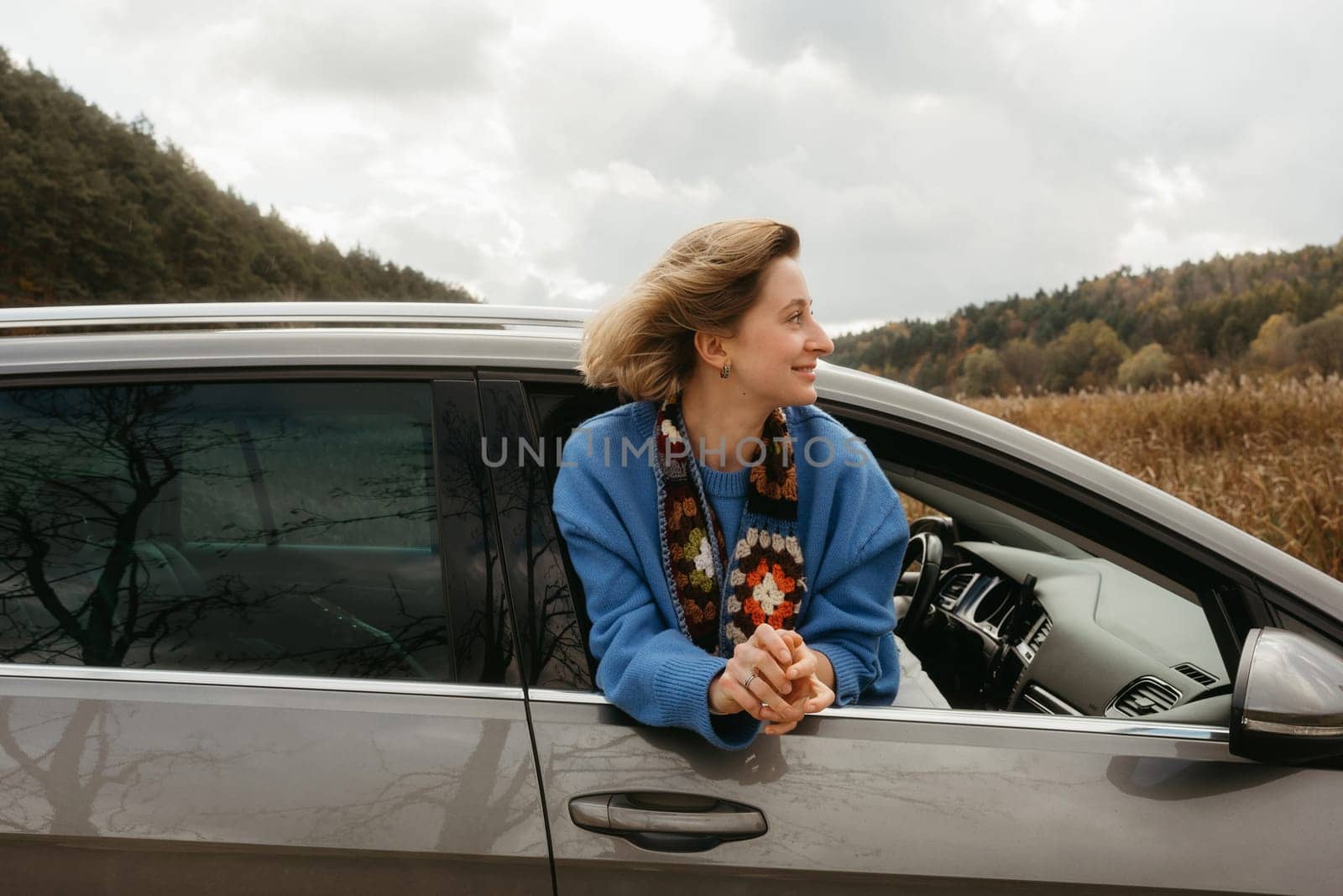 A woman leans out of the car window during road trip in autumn, the wind blows her hair by Romvy