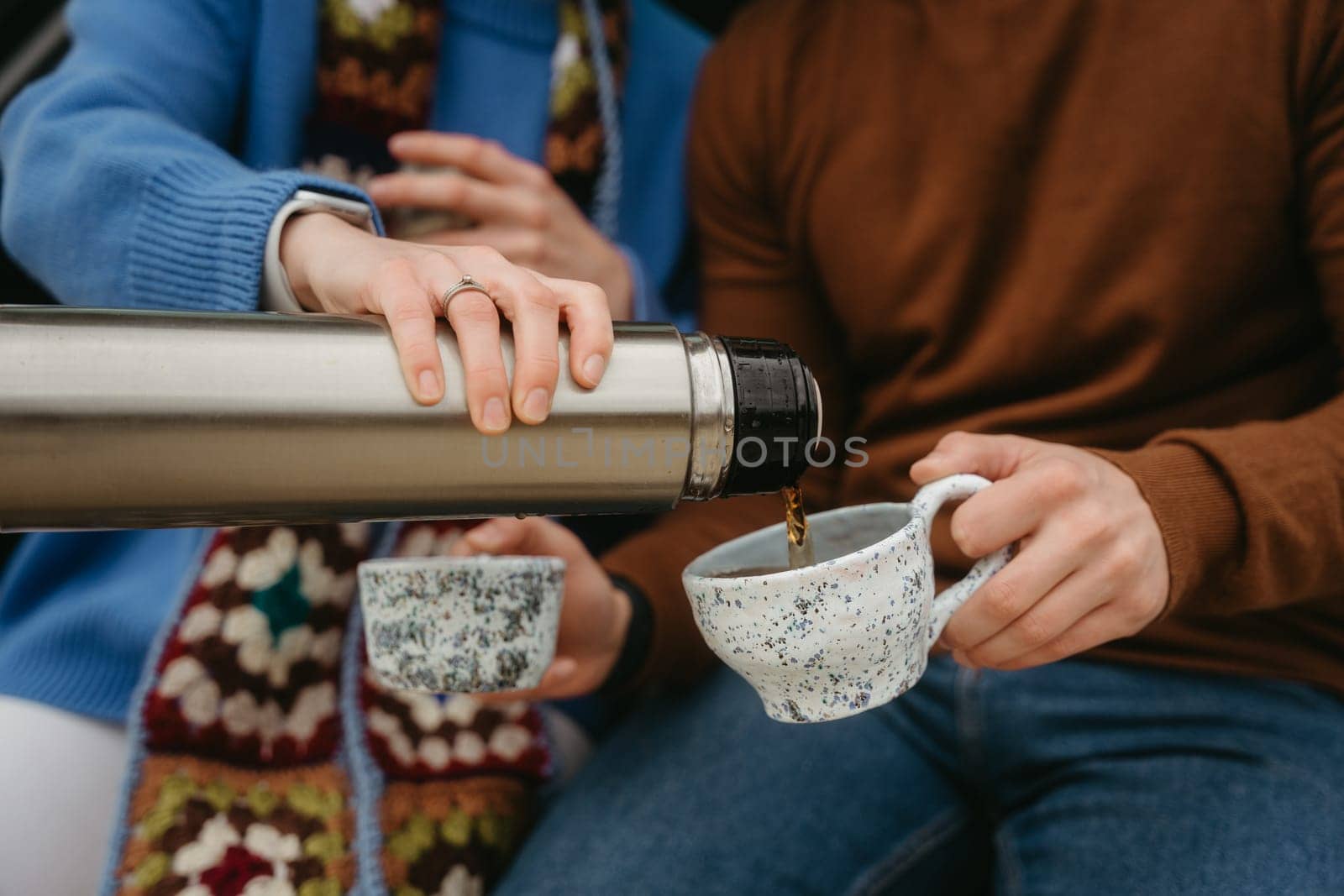 Man and woman drinking tea from thermos during autumn travel, couple holding handmade cups filled with warm drink