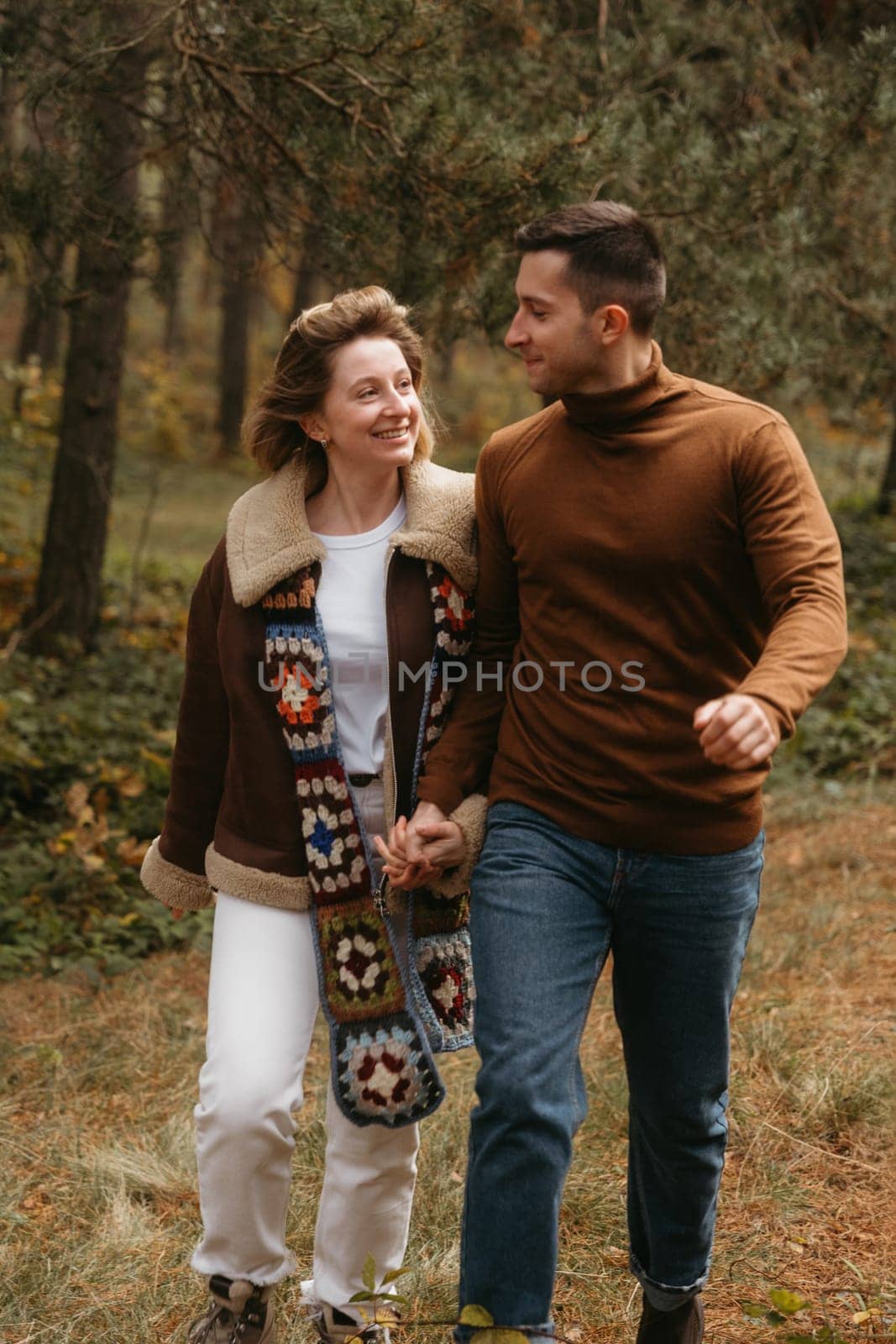 A happy man and woman are walking through the autumn forest, holding hands, adult couple spending time together outdoors by Romvy