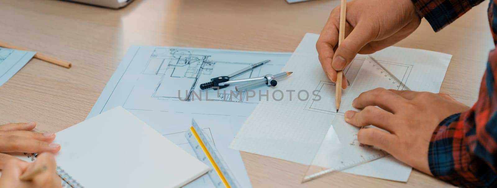 Professional architect hand drawing a blueprint by using ruler measuring length on table with architectural equipment and blue print scatter around at modern office. Closeup. Delineation.