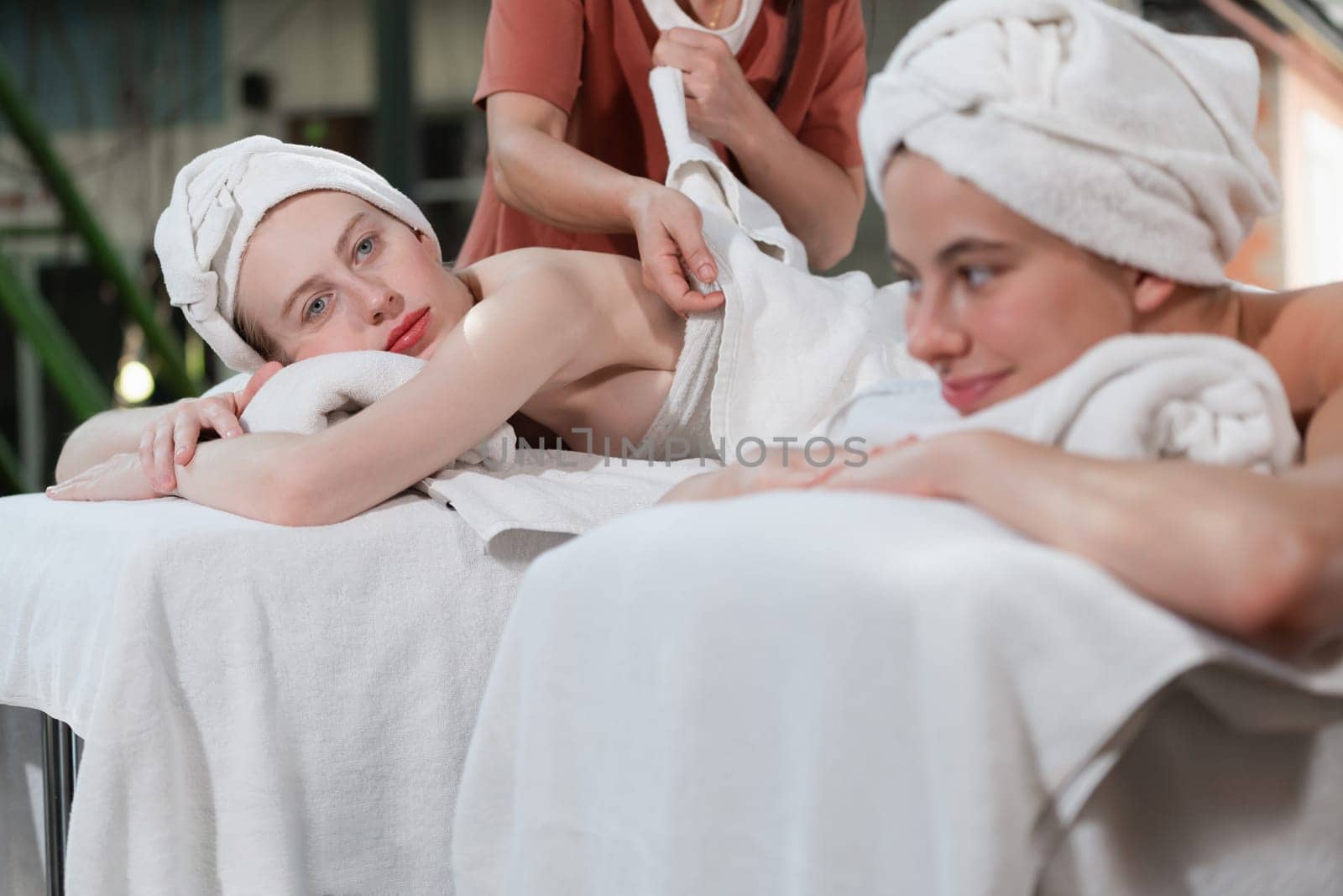 A portrait of a couple of a beautiful young caucasian woman with white towel rest on comfortable spa bed with relaxation while having body massage with professional masseur at spa salon.Tranquility.