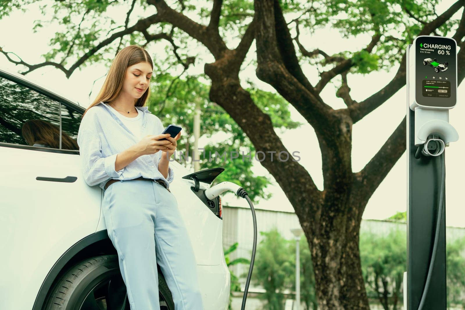 Young woman recharge EV electric vehicle battery from EV charging station. Exalt by biancoblue