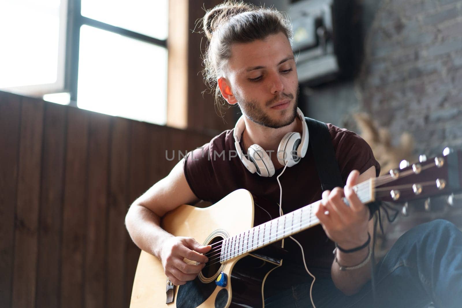 Handsome young man playing acoustic guitar sitting floor living loft room Caucasian male hipster headphones guitar player practicing singing enjoy music relaxing Creative modern young guy Medium shoot