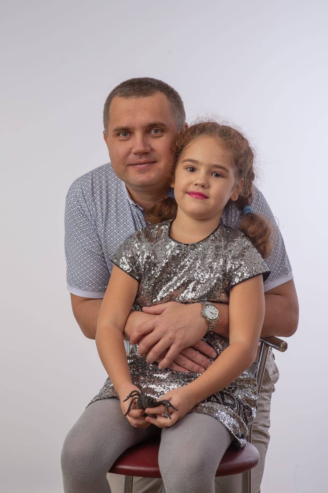 Portrait of lovely daughter smiling and sitting on the neck of her handsome father isolated over gray background