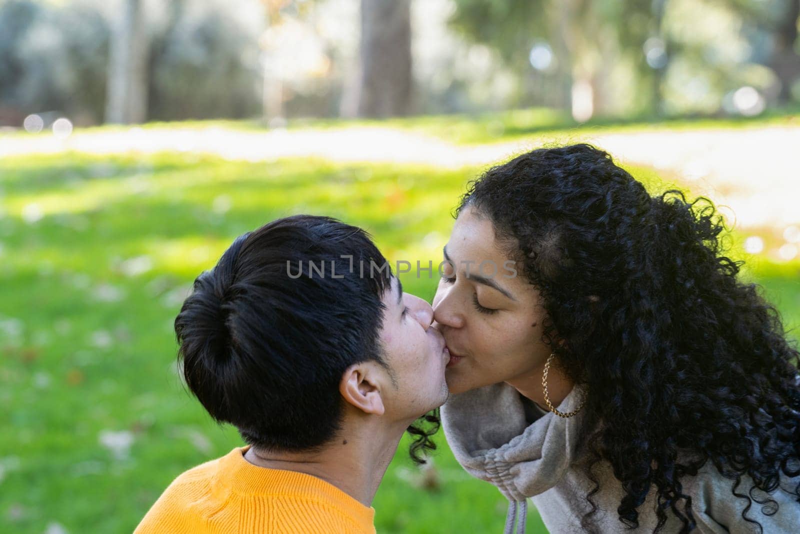 Close up of latin couple kissing under on a green park in a sunny day by papatonic