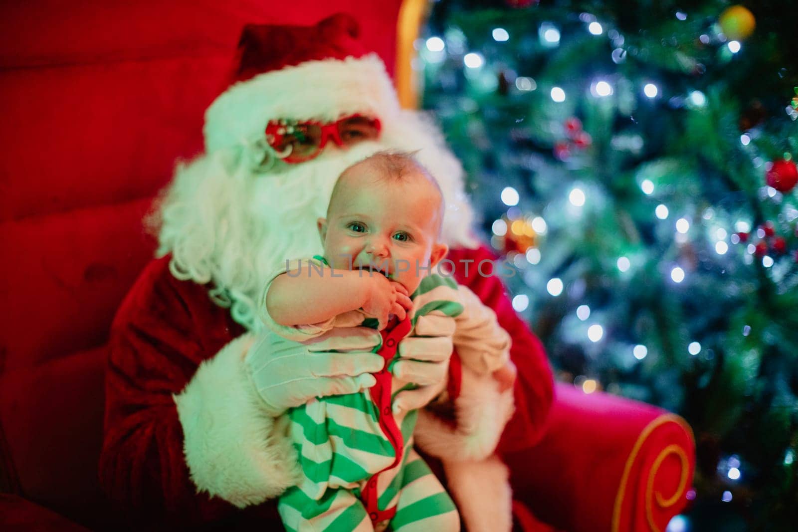 Merry Christmas and happy holidays Cute little child girl and Santa Claus sitting near glowing fir tree. Holiday concept