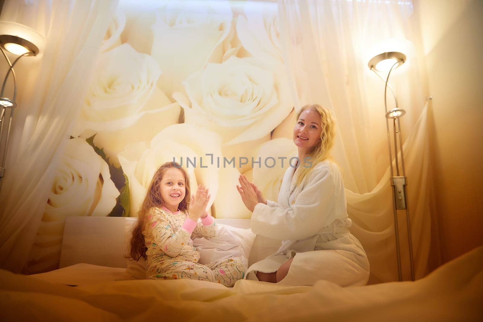 Mother and daughter having relax, fun, play together on a bed in bedroom. The concept of tenderness between mom and girl by keleny