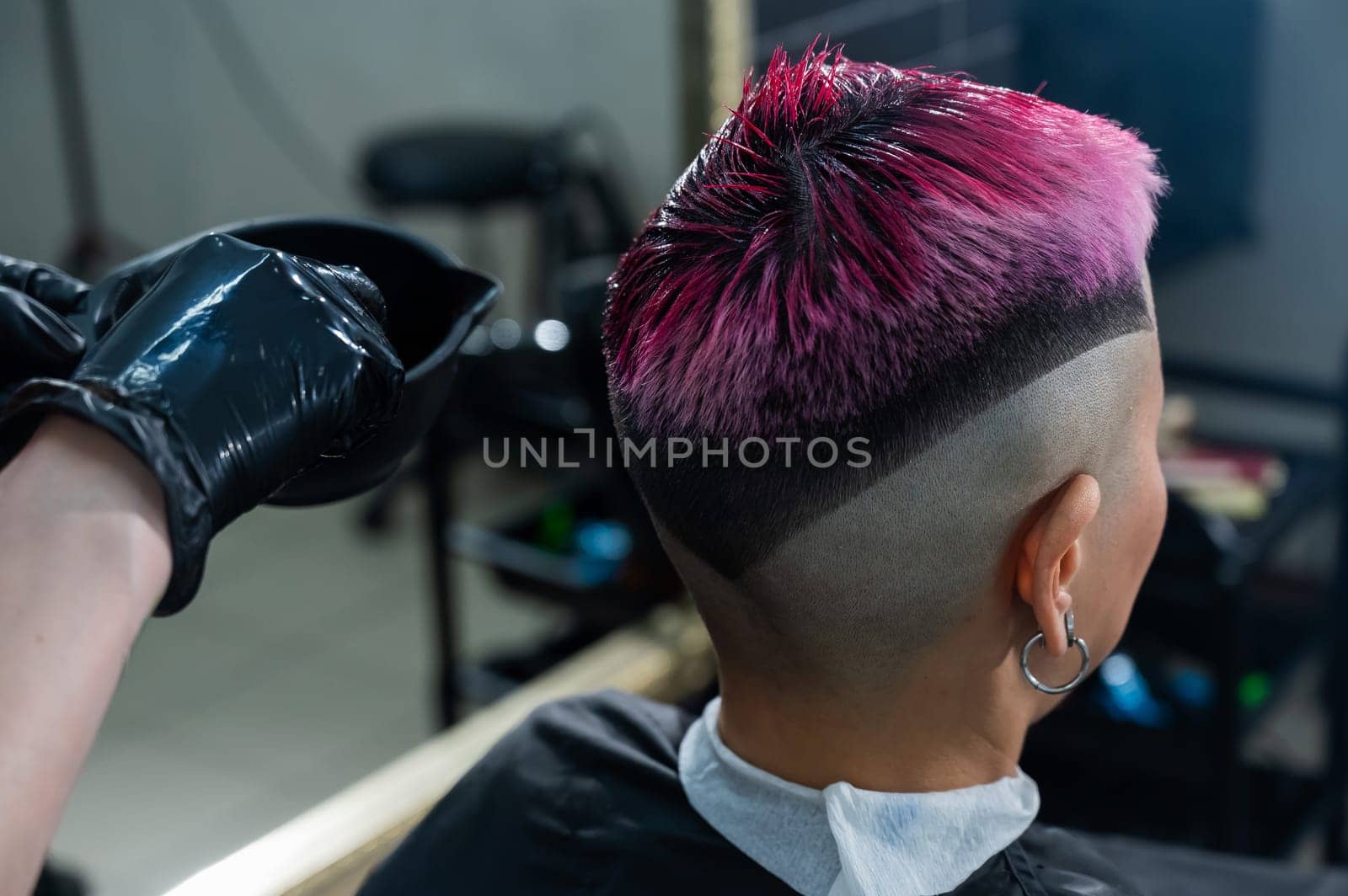 The hairdresser dyes the hair of an Asian woman in pink. Short extreme haircut. by mrwed54