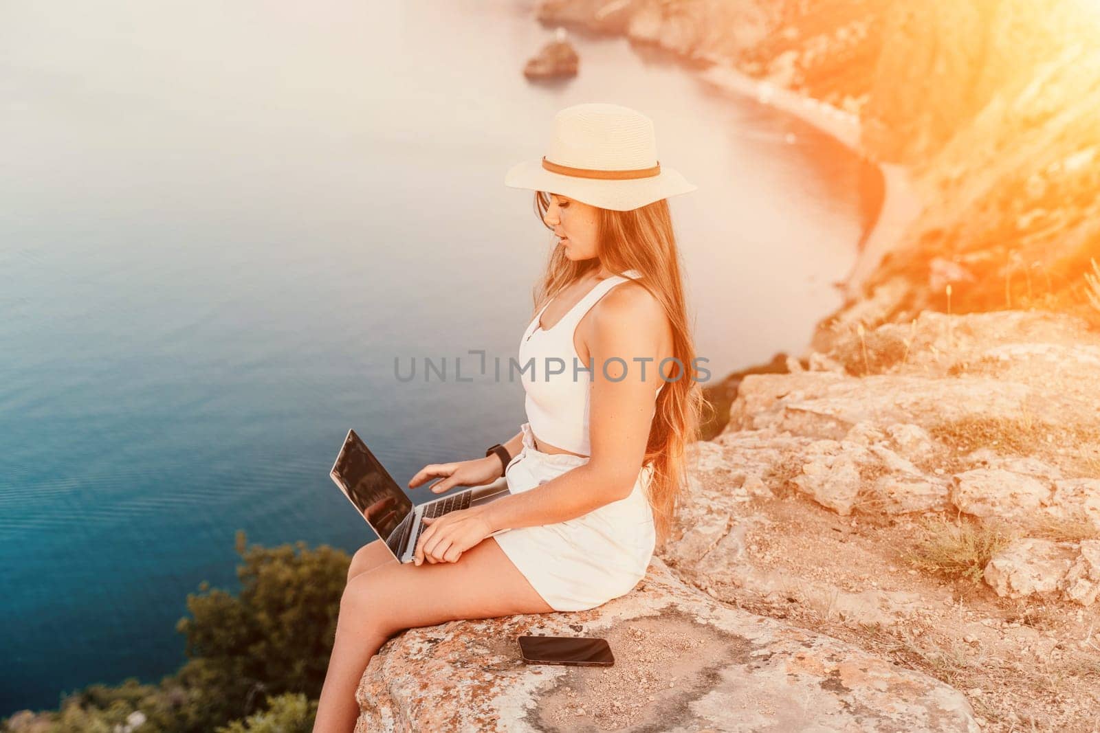 Freelance women sea working on the computer. Good looking middle aged woman typing on a laptop keyboard outdoors with a beautiful sea view. The concept of remote work