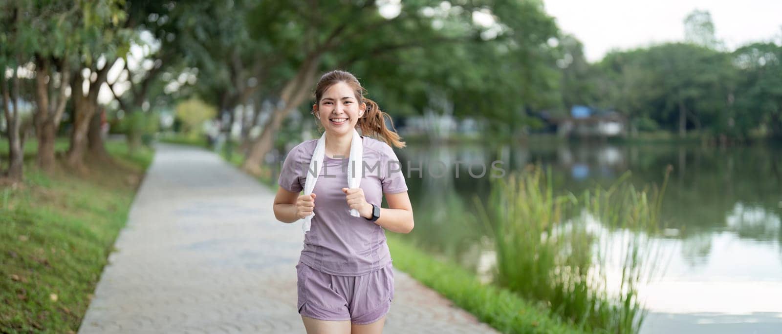 Woman active Asian woman in sportswear listening to music while running or jogging in the park in the morning by nateemee