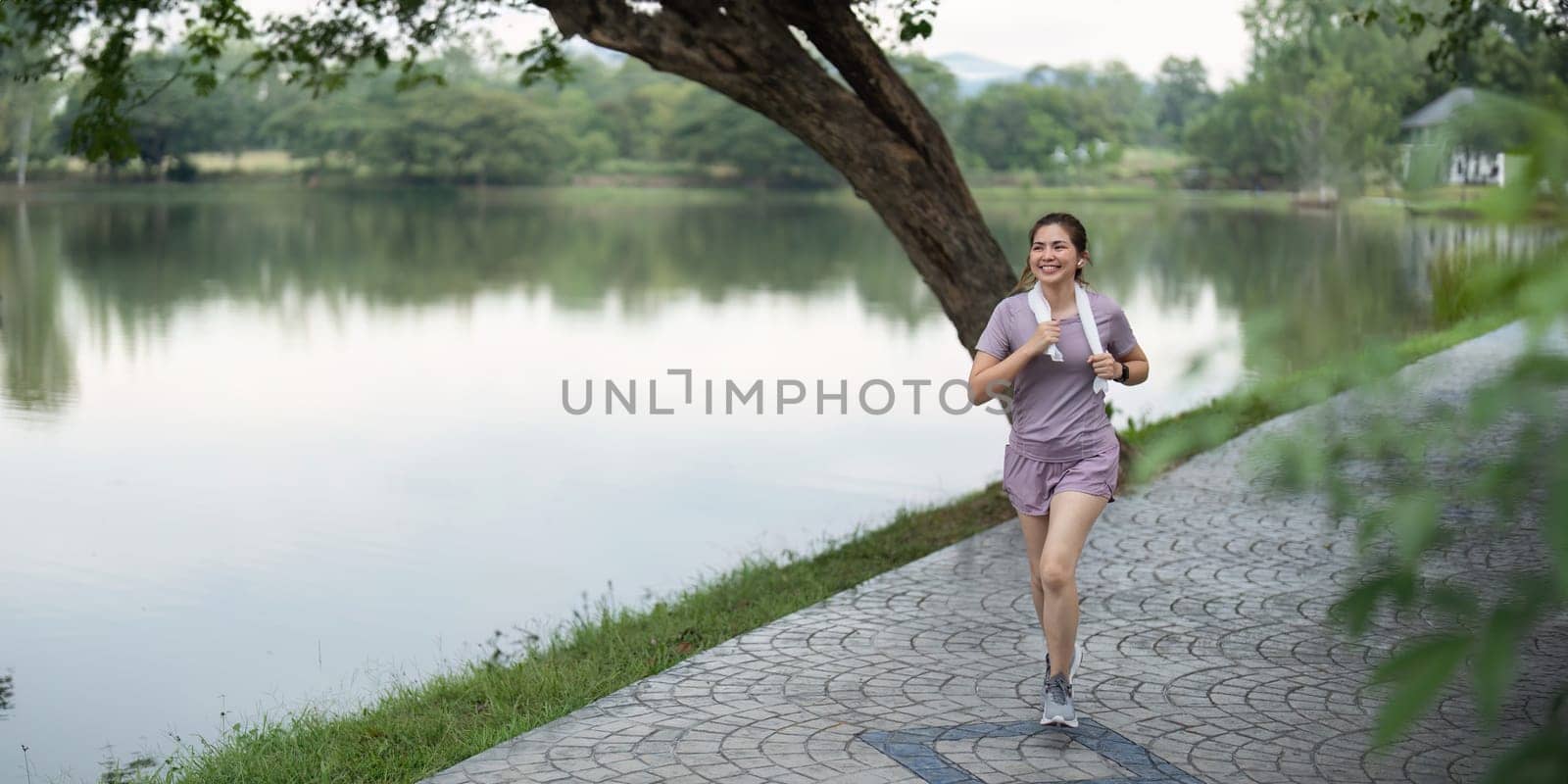 Woman active Asian woman in sportswear listening to music while running or jogging in the park in the morning by nateemee