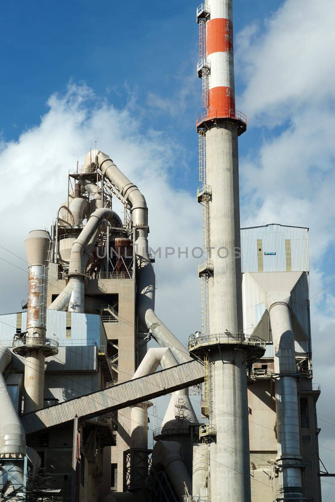 pipes of a cement plant against the background of a cloudy sky close-up by Annado