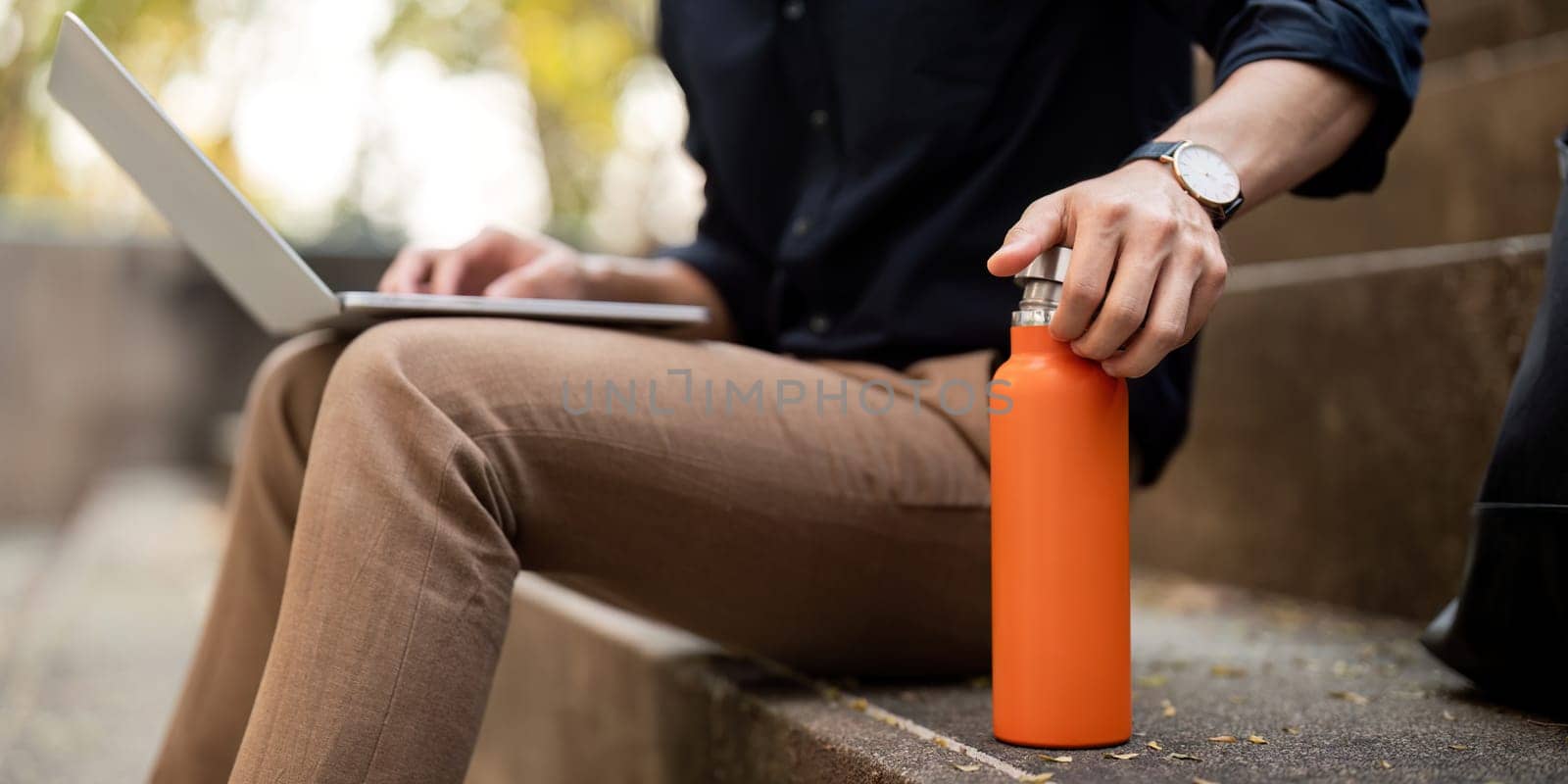 Asian businessman with reusable eco friendly ecological cup using laptop and sitting outside the office building. Eco friendly, sustainable lifestyle concept.