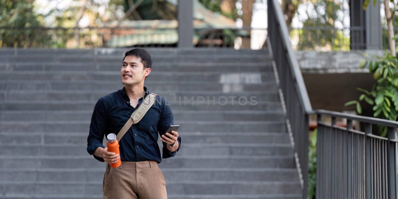 Smiling asian businessman walking to work while to hold reusable eco friendly ecological cup in the city.