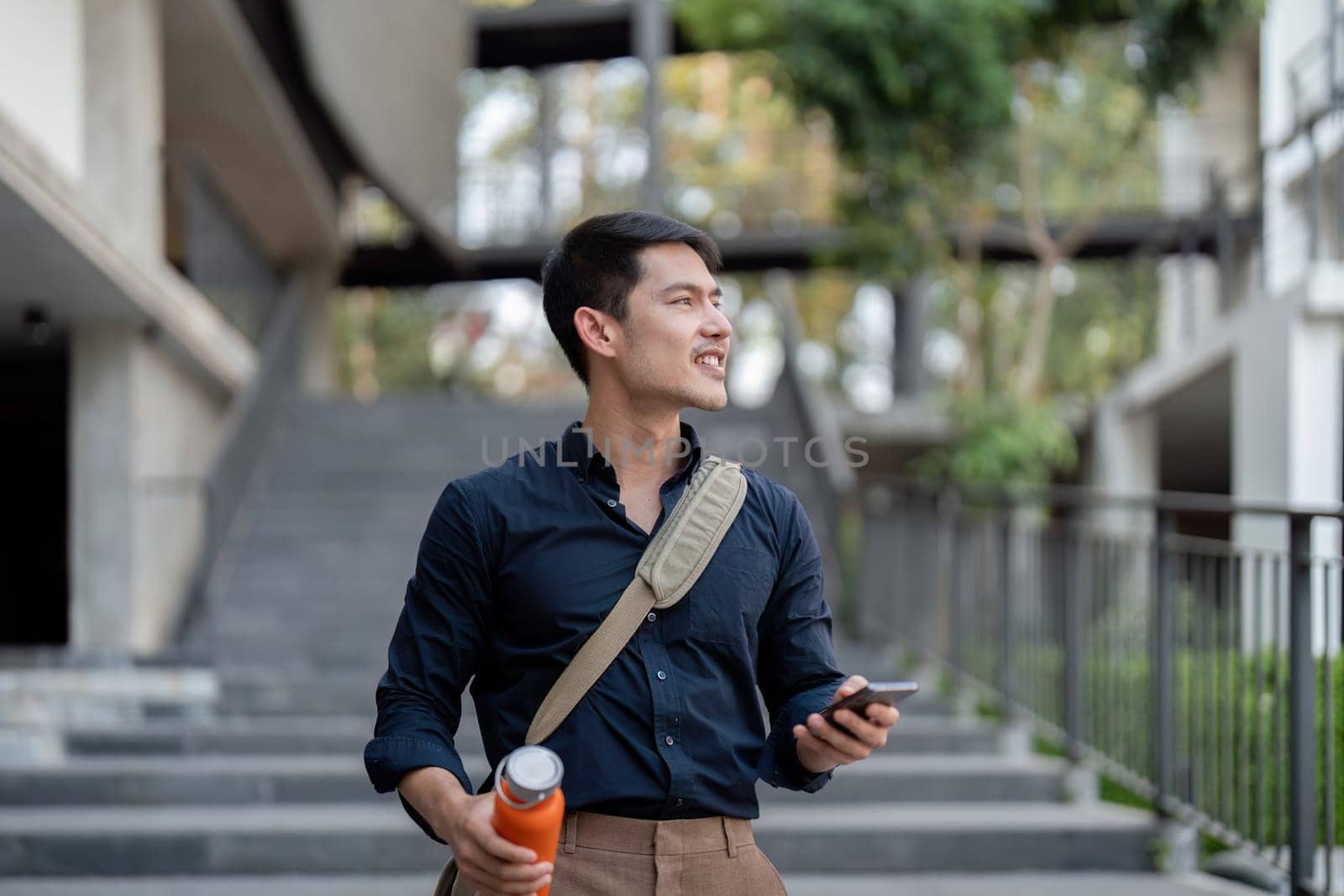 Smiling asian businessman walking to work while to hold reusable eco friendly ecological cup in the city by nateemee