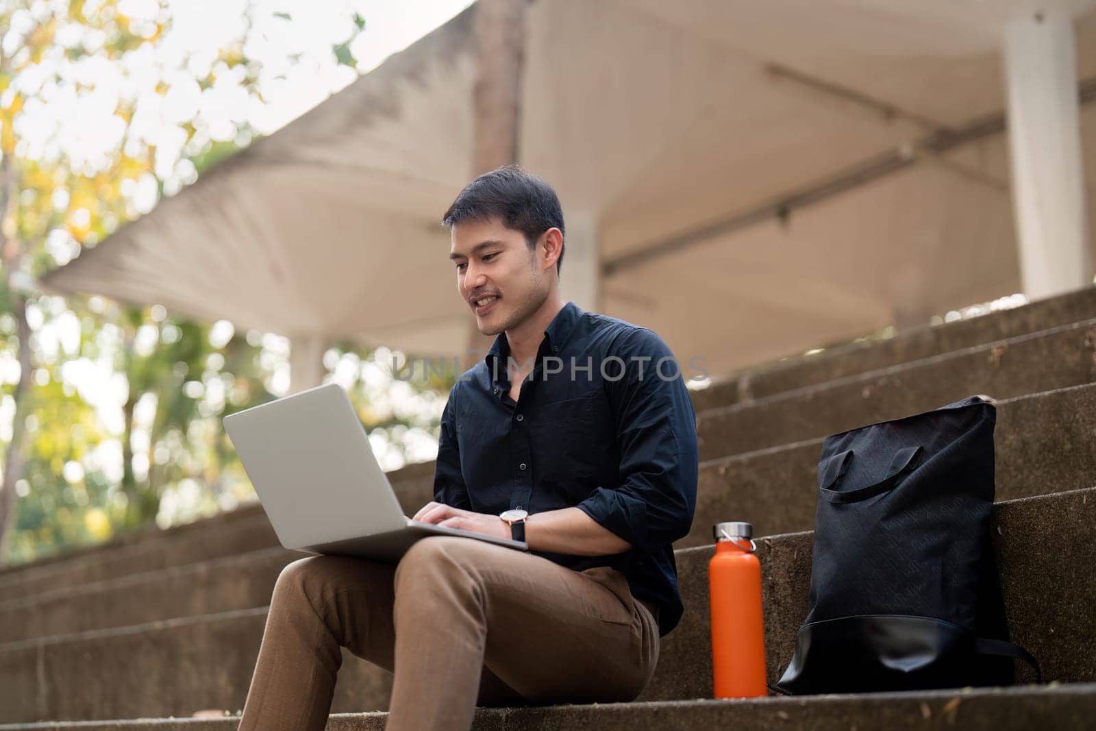 Asian businessman with reusable eco friendly ecological cup using laptop and sitting outside the office building. Eco friendly, sustainable lifestyle concept by nateemee