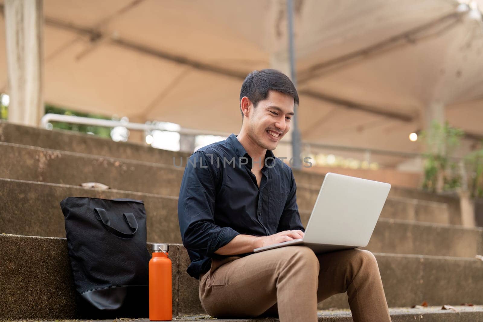 Asian businessman with reusable eco friendly ecological cup using laptop and sitting outside the office building. Eco friendly, sustainable lifestyle concept.