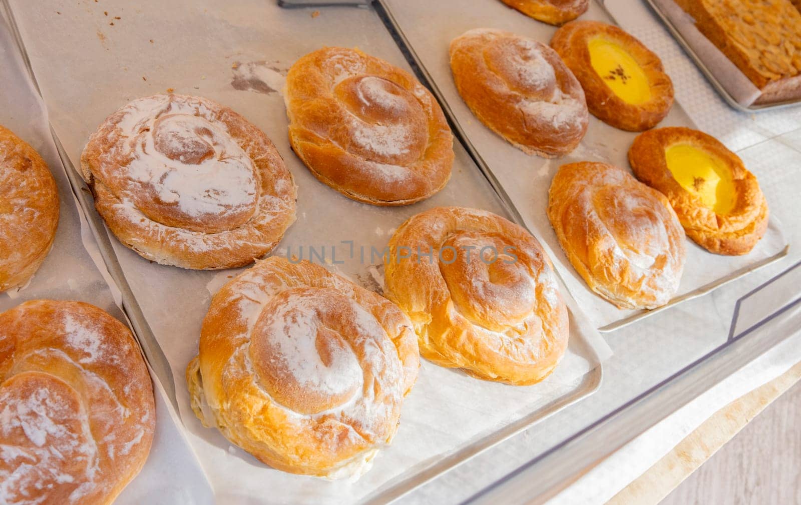 Flaky ensaimada pastries, one filled with bright yellow cream, on parchment