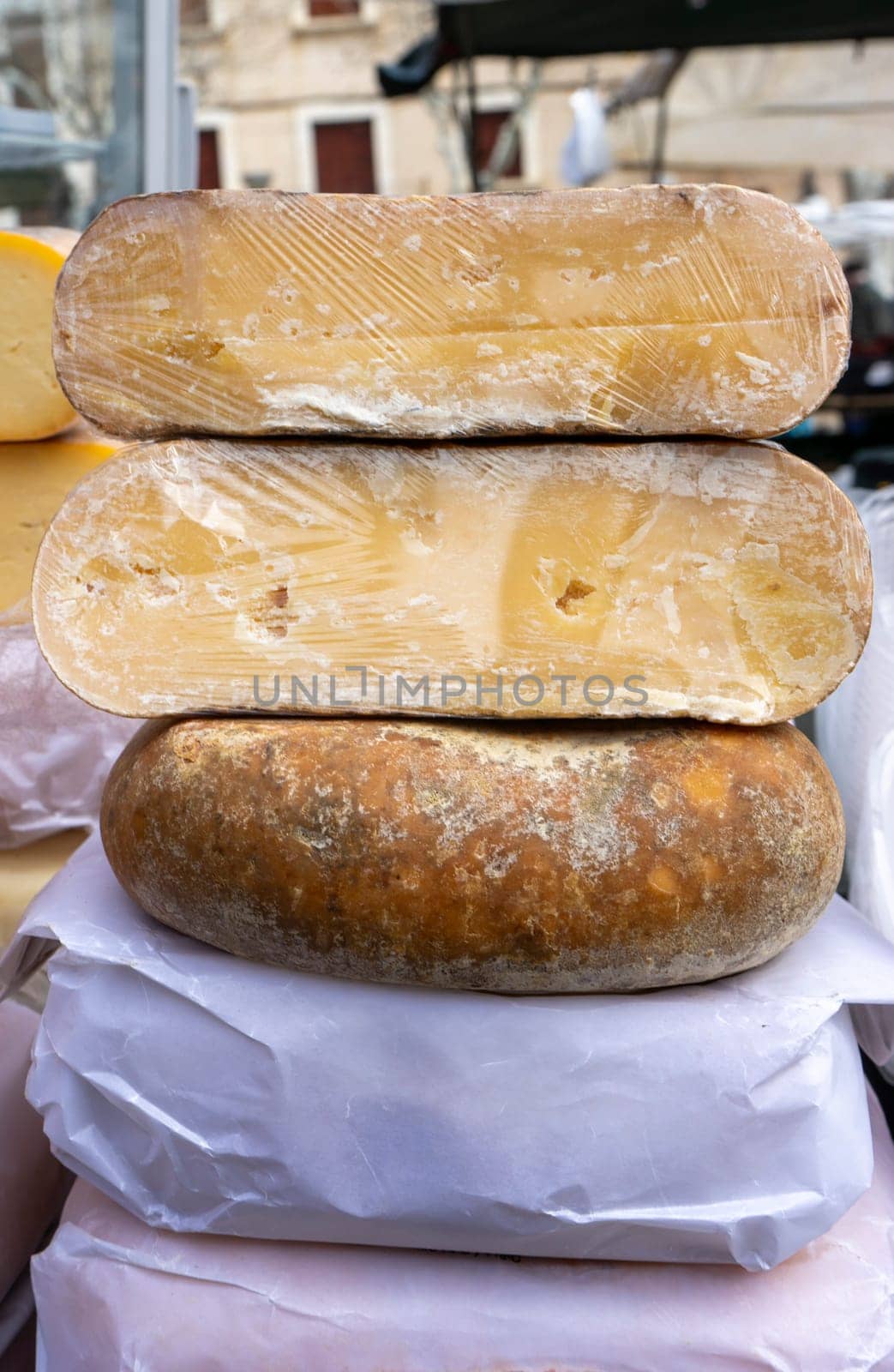 Three mature cheese wheels, showcasing the art of traditional cheese-making, are stacked, ready to entice gourmands at a local market.