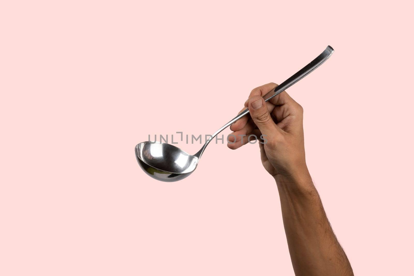 Black male hand holding a silver kitchen ladle isolated o pink background by TropicalNinjaStudio