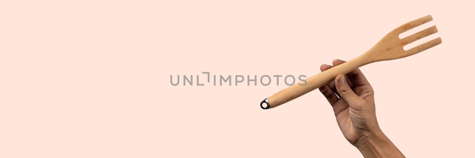 Hand holding wooden fork on light pink background. High quality photo.