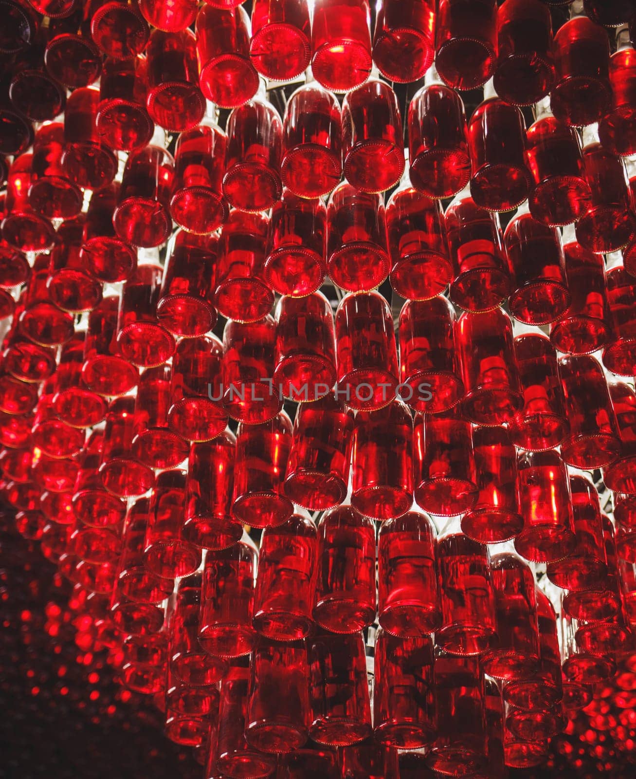 Many bottles of red wine stacked on top of each other, illuminated by light