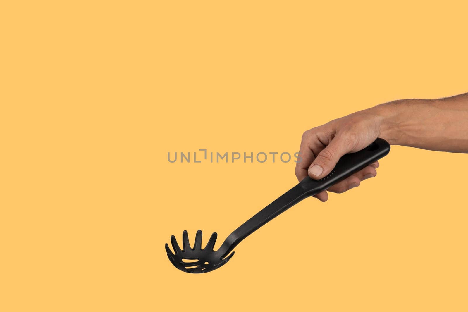 Black male hand holding plastic kitchen skimmer on yellow background. by TropicalNinjaStudio