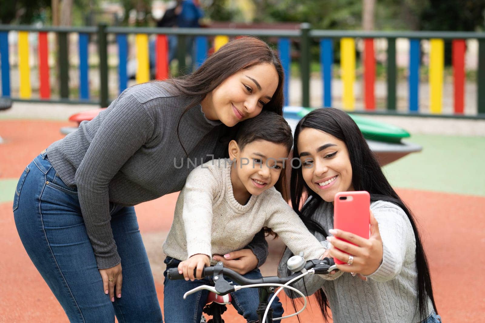 Happy smiling lesbian mothers taking a selfie with their son in a playground by papatonic