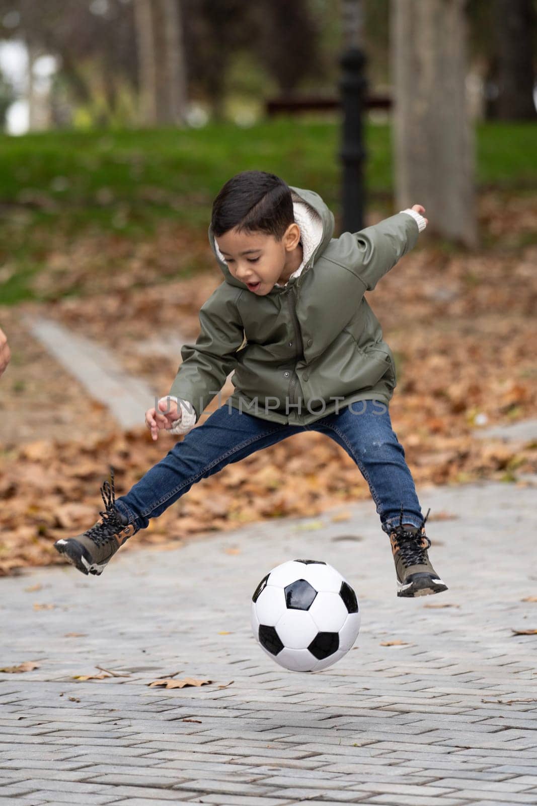 Happy kid with soccer ball jumping outdoors in a public park.