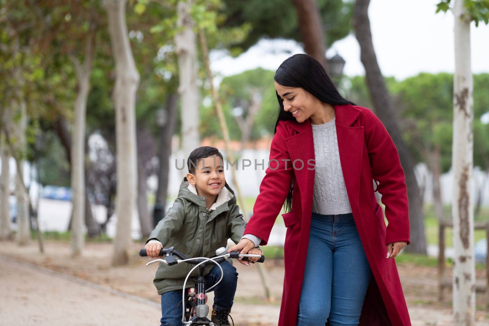 Mother is teaching her son how to ride a bicycle. Son learning to ride a bike. Family fun time.