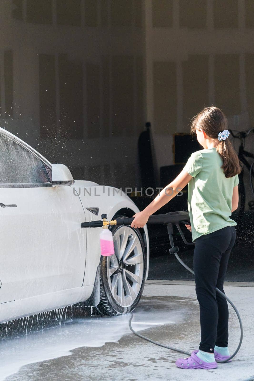 Denver, Colorado, USA-September 1, 2023-A young girl enthusiastically assists in washing the family's electric car in their suburban driveway.