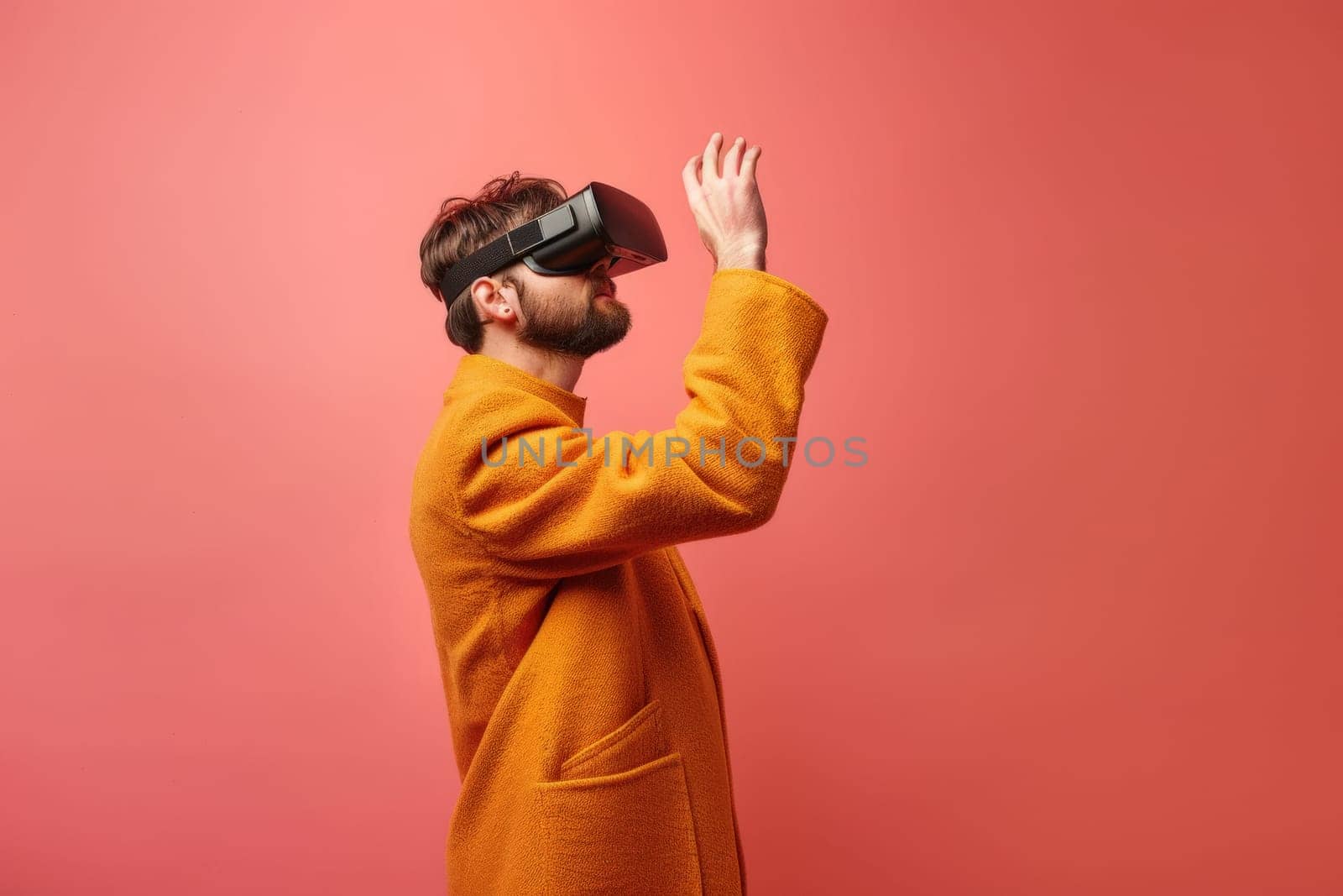 A man in a yellow coat is wearing a virtual reality headset. He is looking up and he is in a playful mood