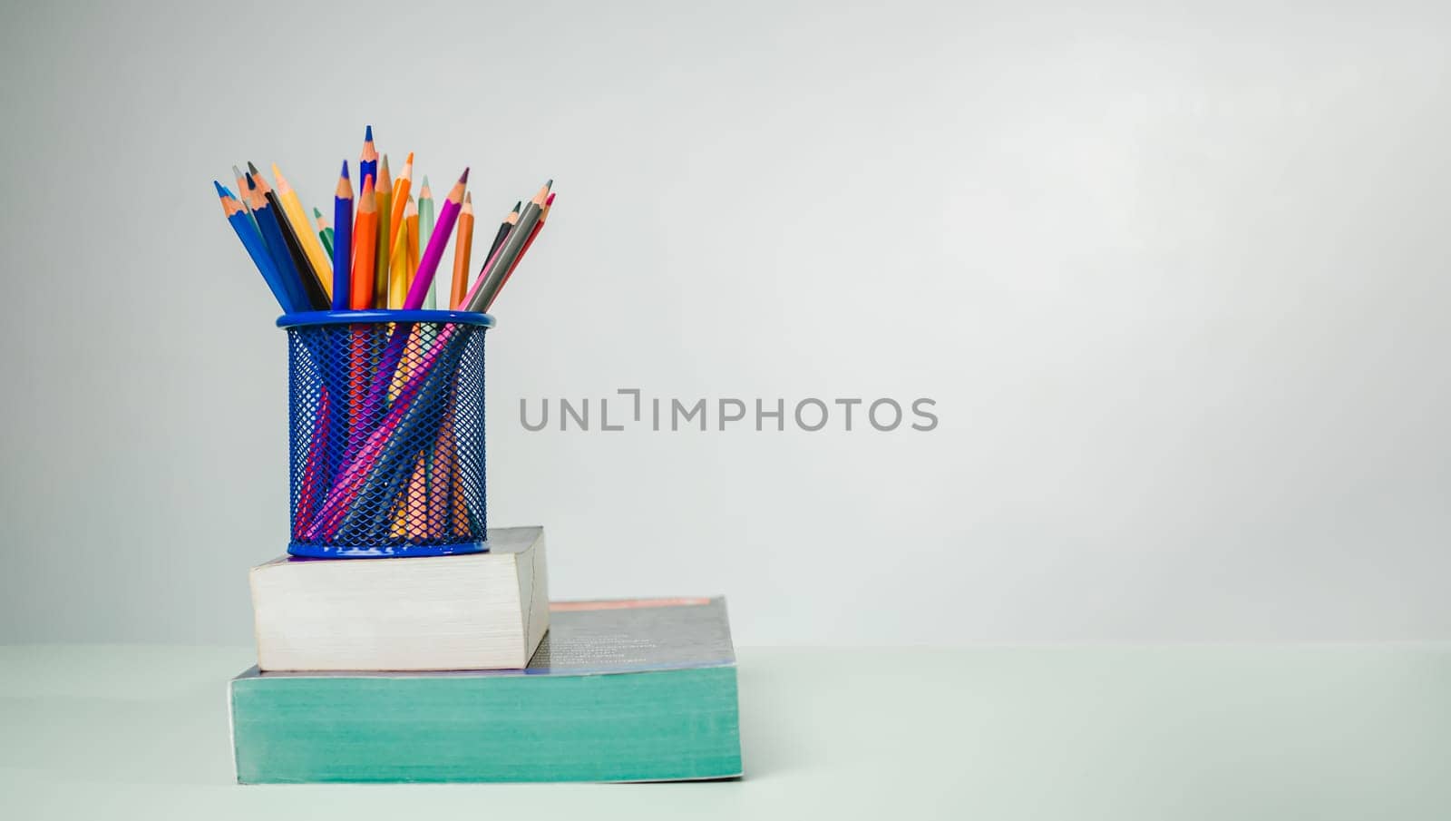 Stack of colorful textbooks and a glass of bright pencils on a white background, Concept of education, training, School tools, workspace, copy space, Banner design education concept background. by Unimages2527