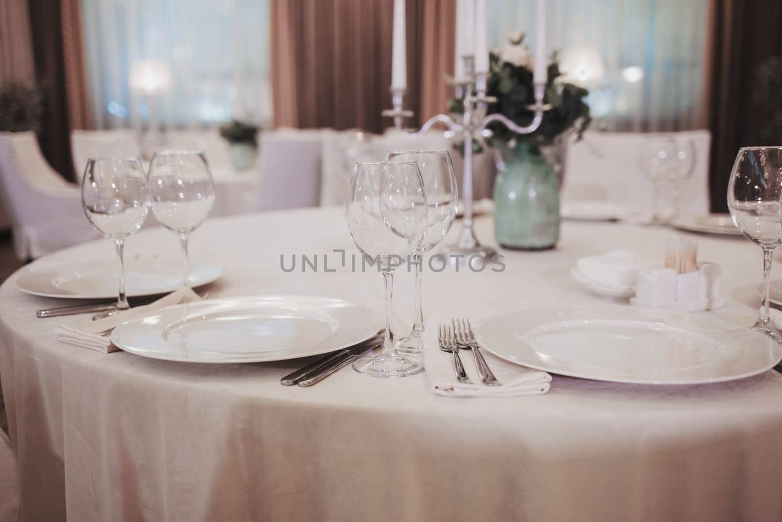 restaurant interior. White table setting. Elegant empty plate, cutlery, napkin and glasses for vine.