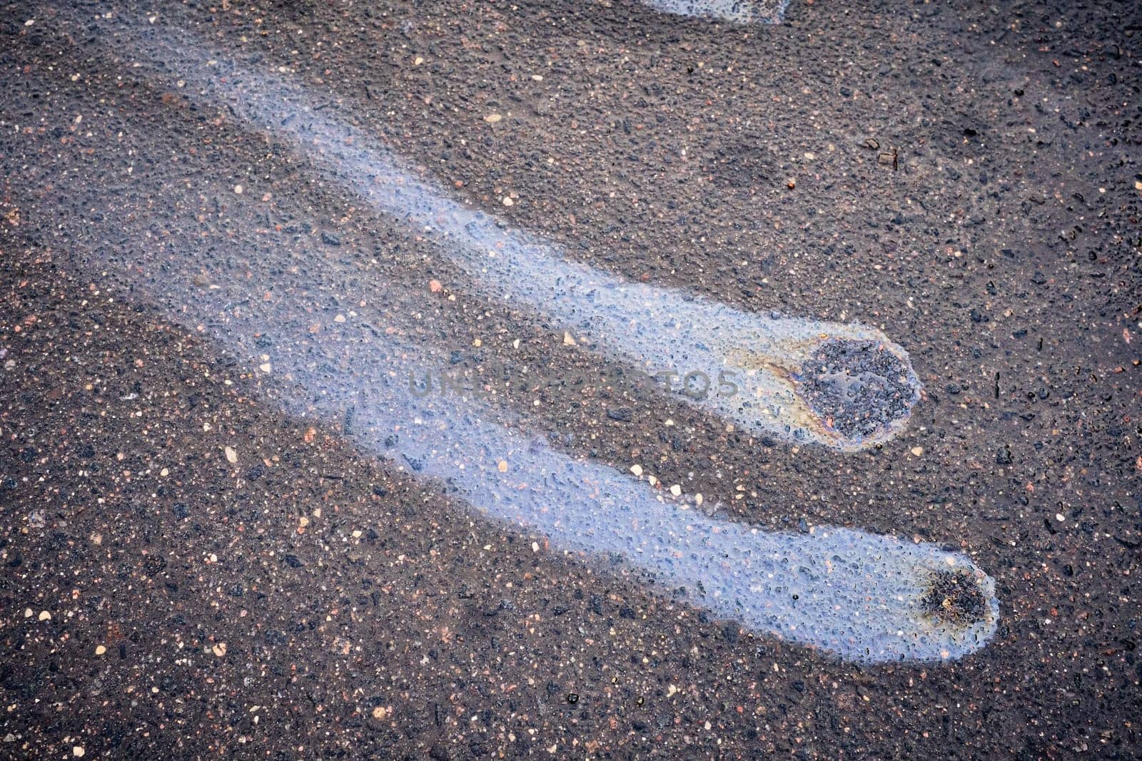 Rain blurred car oil from a malfunctioning car in a parking lot. Texture of asphalt and rainbow stains. Environmental pollution concept.