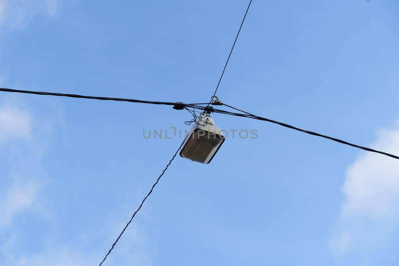 A streetlight hangs from a wire against a clear blue sky, illuminating the street below.