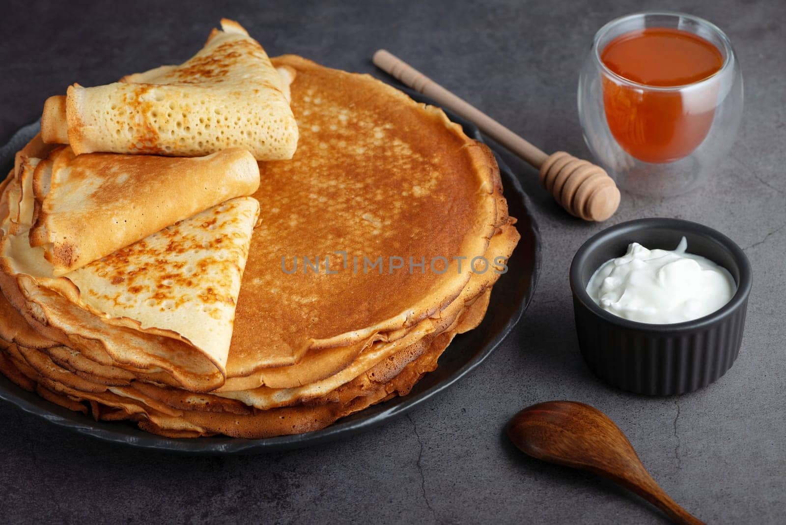Stack of russian thin pancakes blini with fresh sour cream and honey.