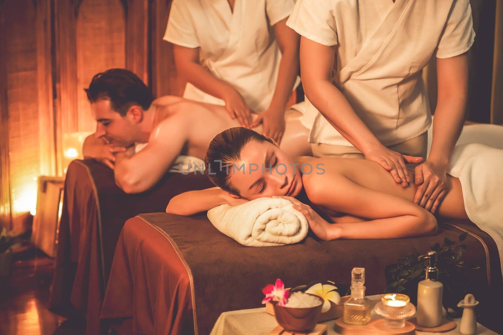 Caucasian couple customer enjoying relaxing anti-stress spa massage and pampering with beauty skin recreation leisure in warm candle lighting ambient salon spa at luxury resort or hotel. Quiescent