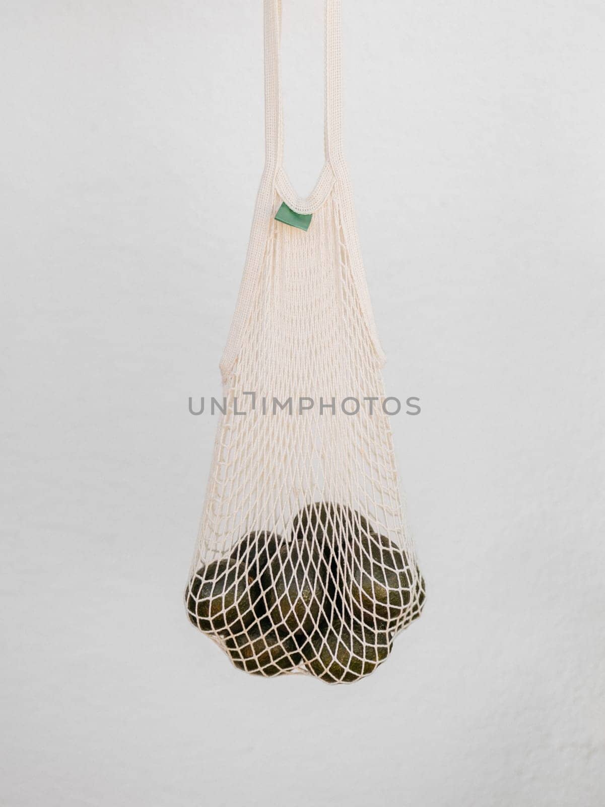 A Net Bag Filled With A Bunch Of avocado on white background by apavlin