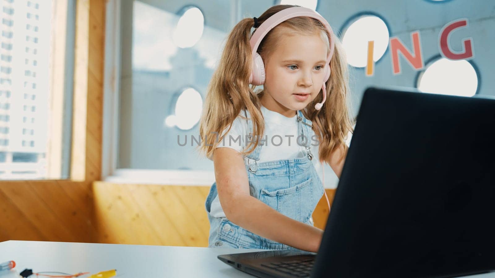 Young student working on laptop or studying in online classroom. Caucasian girl typing on laptop while doing homework or listening music.Little kid wearing headphone. Creative learning. Erudition.