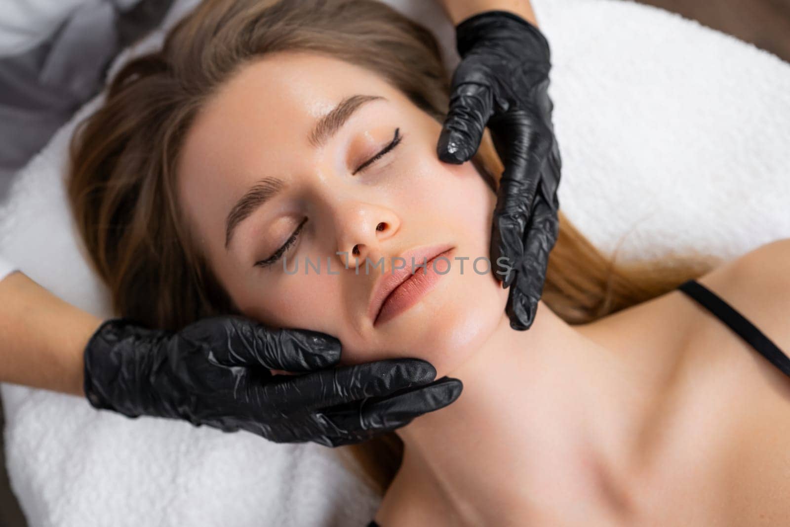 Top view of womans hands massaging female client facial skin at beauty salon