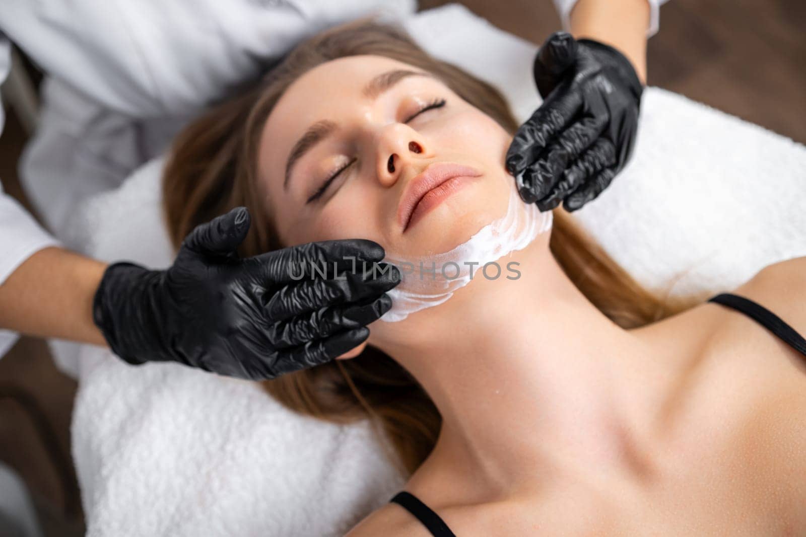 Enjoying a rejuvenating experience, a beautiful young woman receives a face lifting massage at the beauty salon.