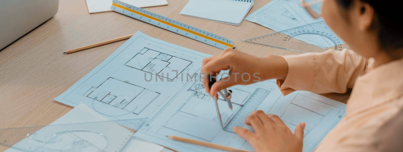 Professional architect drawing blueprint by using divider on the table with stationary and architectural document scatter around at architectural office. Closeup. Focus on hand. Delineation.