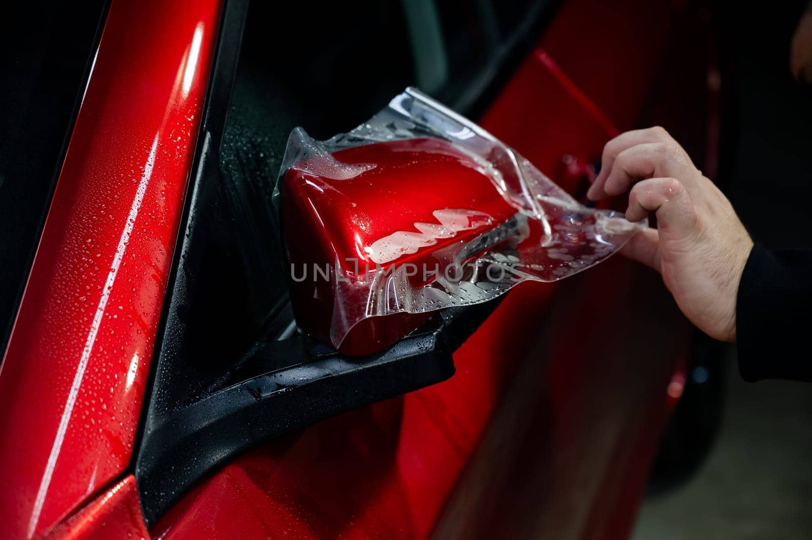 The master applies vinyl film to the side view mirror of a car