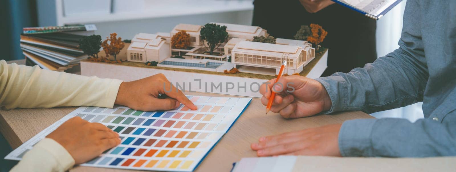 Cropped image of professional interior design team discuss about color and material usage for the project while project manager choose main theme color with house model on meeting table. Variegated.