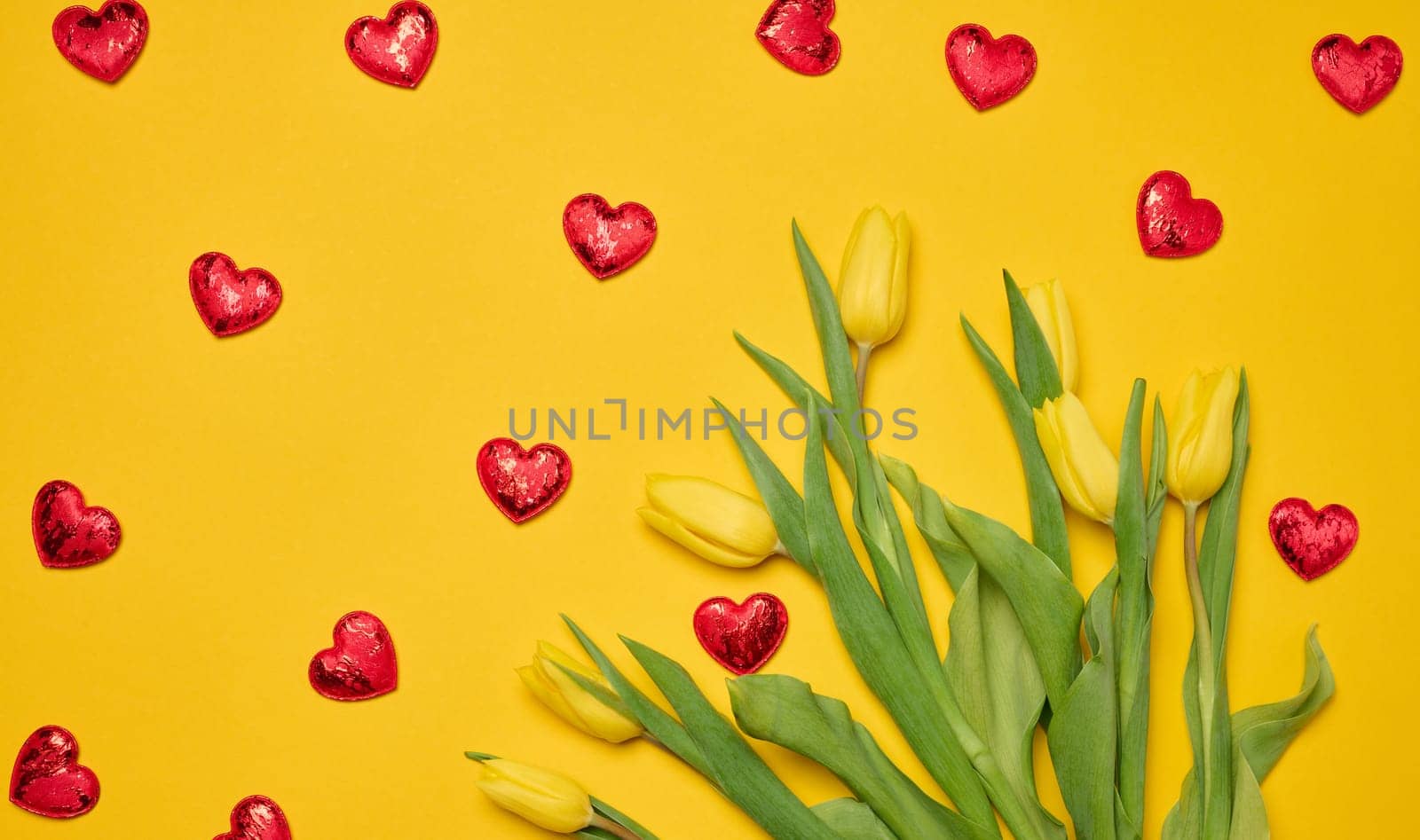 Bouquet of blooming yellow tulips with green leaves on a yellow background, top view