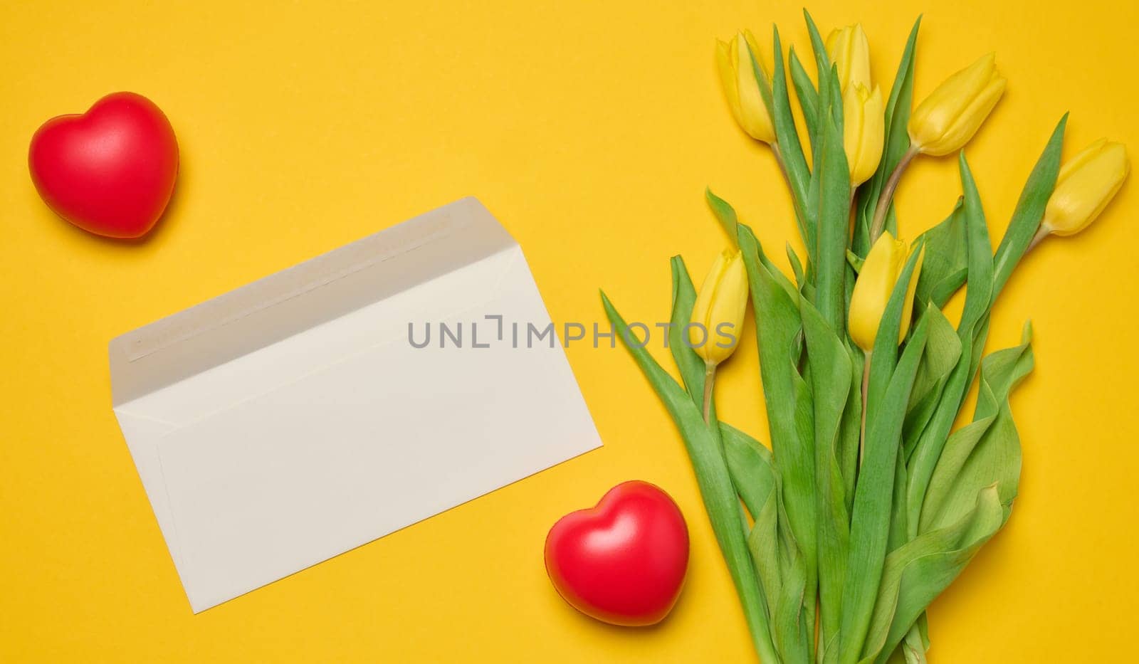Envelope and red heart and bouquet of blooming tulips with green leaves on a yellow background by ndanko