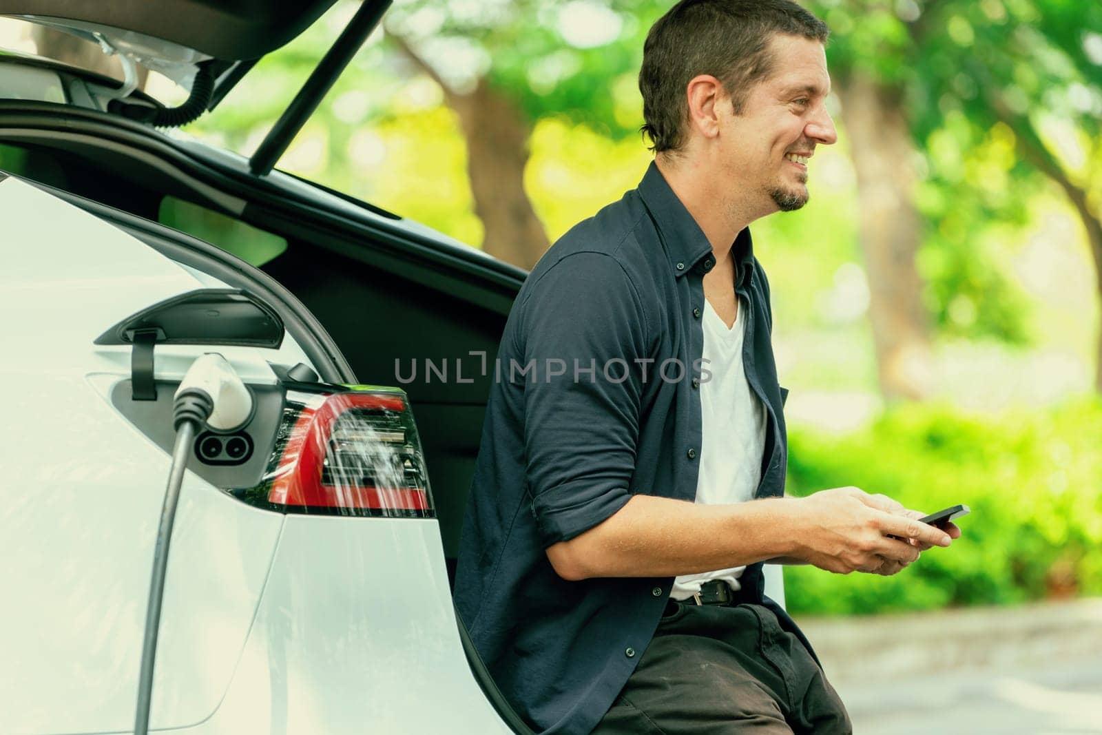 Man using smartphone to pay for electric car charging. Exalt by biancoblue