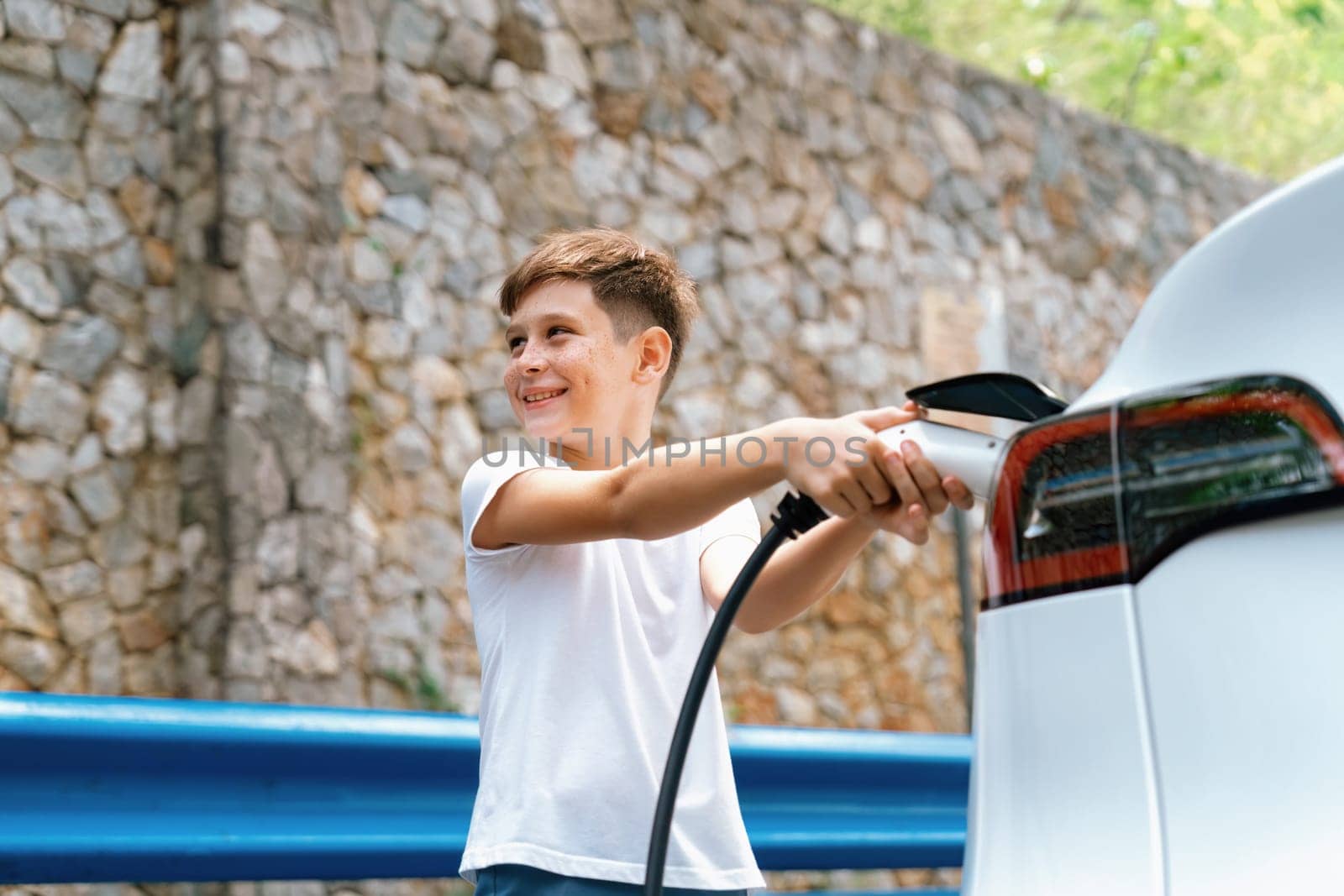 Little boy recharging eco-friendly electric car from EV charging station. EV car road trip travel concept for alternative transportation powered by clean renewable and sustainable energy. Perpetual